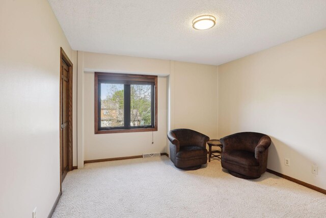 living area with light carpet, a textured ceiling, visible vents, and baseboards