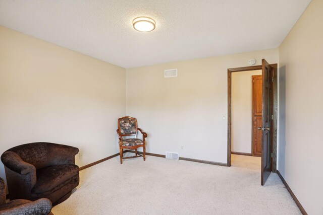 living area featuring baseboards, visible vents, a textured ceiling, and light colored carpet