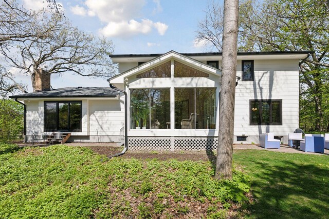 rear view of house featuring a sunroom, a lawn, and a chimney