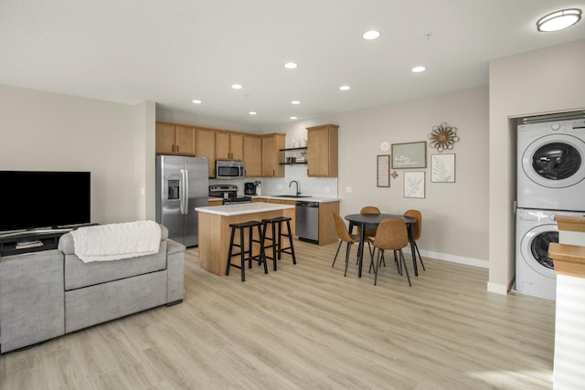 kitchen with a kitchen breakfast bar, stacked washer and dryer, light wood-type flooring, a kitchen island, and stainless steel appliances