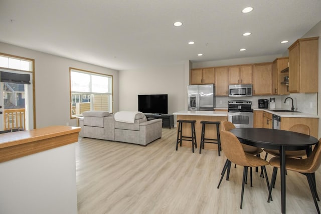 kitchen featuring sink, a center island, stainless steel appliances, light hardwood / wood-style flooring, and a breakfast bar area