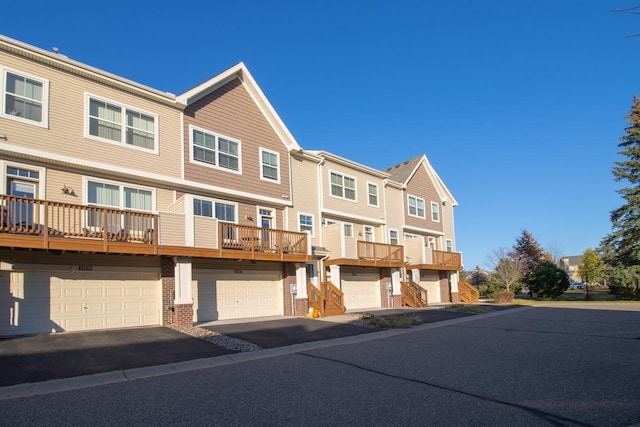 view of property with driveway, a balcony, a residential view, an attached garage, and brick siding