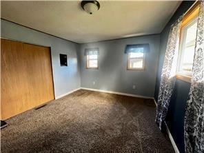 unfurnished bedroom featuring a closet, multiple windows, and dark colored carpet