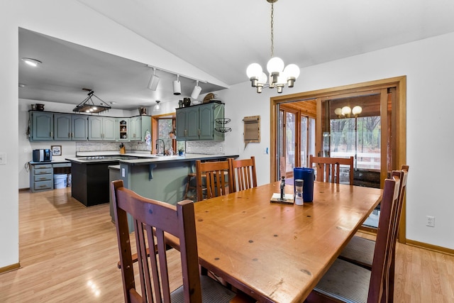 dining room featuring lofted ceiling, sink, a chandelier, and light hardwood / wood-style floors