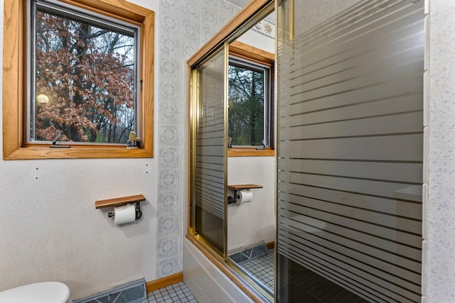 bathroom with tile patterned flooring, shower / bath combination with glass door, and toilet