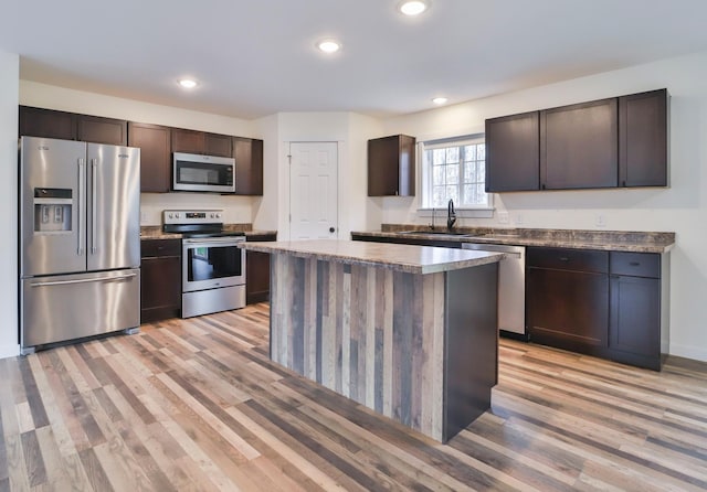 kitchen featuring stainless steel appliances, sink, dark brown cabinets, a kitchen island, and light wood-type flooring