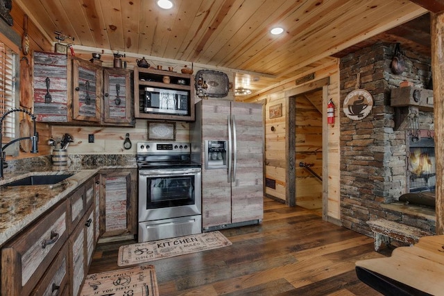 kitchen with sink, appliances with stainless steel finishes, stone counters, wooden walls, and dark hardwood / wood-style flooring