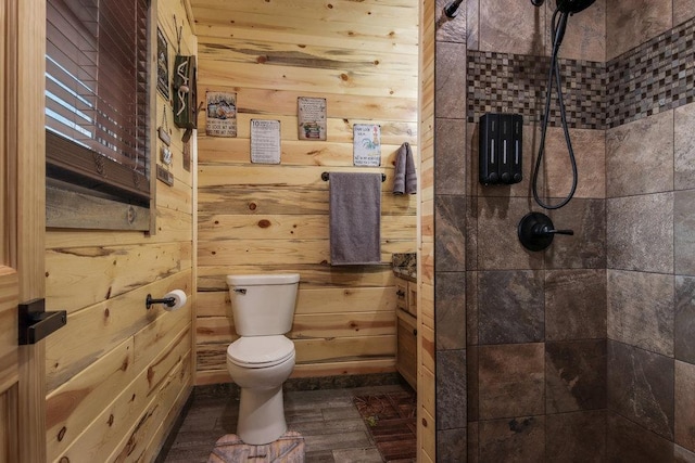 bathroom with hardwood / wood-style flooring, a tile shower, wooden walls, and toilet