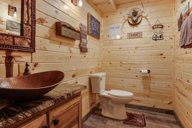 bathroom with toilet, vanity, wooden walls, and wood-type flooring