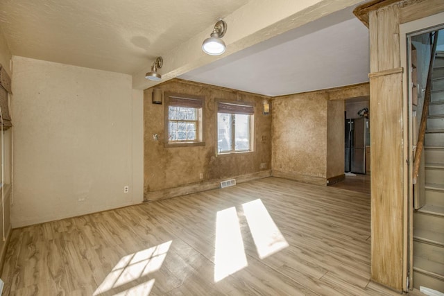 spare room featuring stairway, wood finished floors, and visible vents