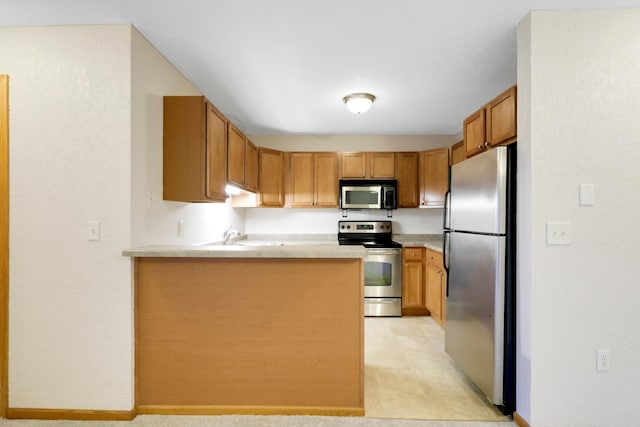 kitchen featuring stainless steel appliances, a peninsula, a sink, light countertops, and brown cabinets