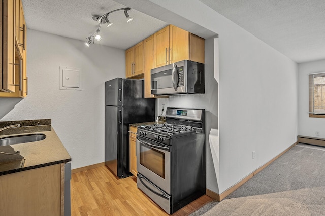 kitchen with light wood-type flooring, appliances with stainless steel finishes, a textured ceiling, sink, and a baseboard heating unit