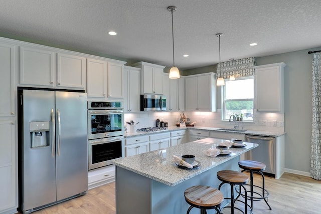 kitchen with stainless steel appliances, light wood-type flooring, white cabinetry, sink, and a center island