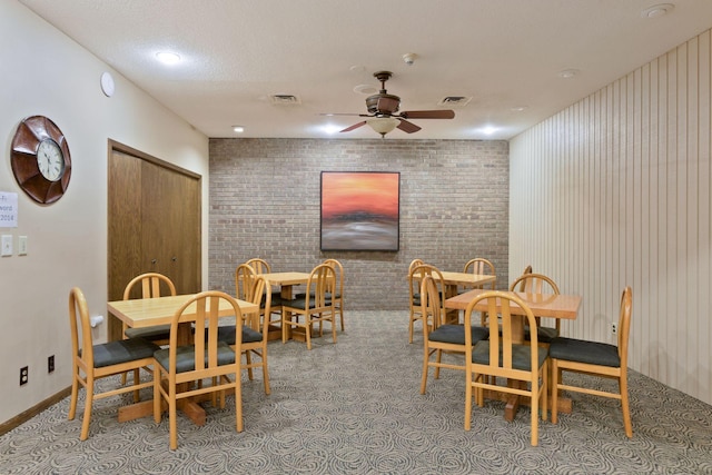 dining space featuring ceiling fan, brick wall, light carpet, and a textured ceiling