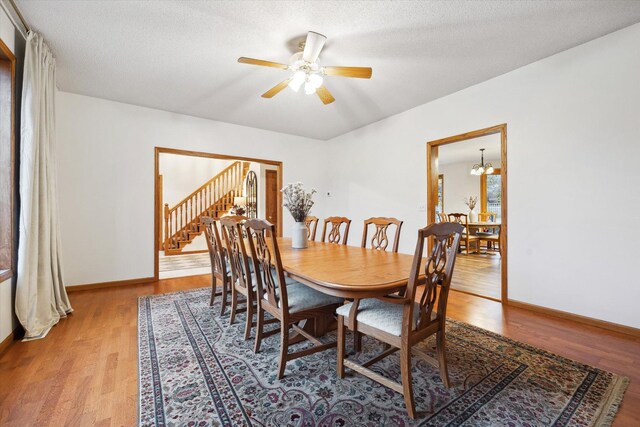 dining space with ceiling fan with notable chandelier, wood-type flooring, and a textured ceiling