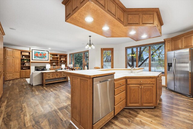 kitchen featuring appliances with stainless steel finishes, dark hardwood / wood-style floors, an inviting chandelier, a kitchen island with sink, and pendant lighting