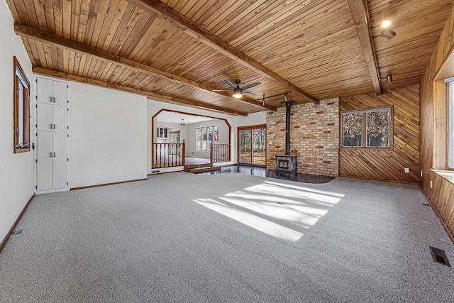 unfurnished living room featuring a wood stove, wood walls, beamed ceiling, and wood ceiling