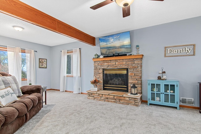 living room featuring a stone fireplace, beamed ceiling, carpet flooring, ceiling fan, and a textured ceiling