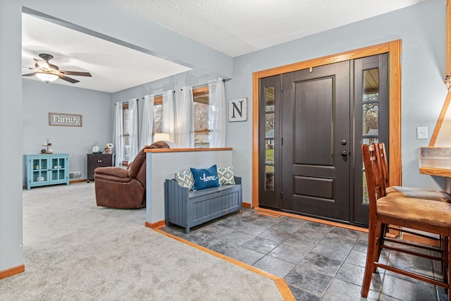 carpeted foyer entrance with a ceiling fan, a healthy amount of sunlight, baseboards, and a textured ceiling