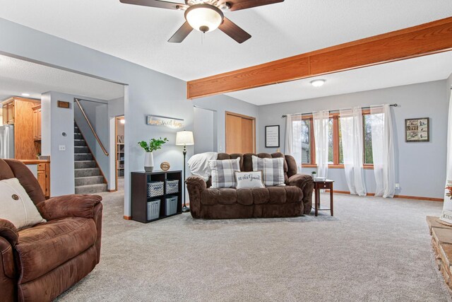 living room featuring stairway, baseboards, ceiling fan, beamed ceiling, and light colored carpet