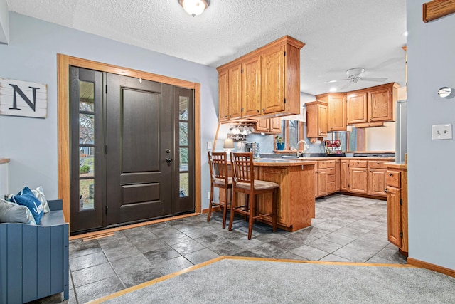 kitchen with a breakfast bar, a textured ceiling, a peninsula, baseboards, and ceiling fan