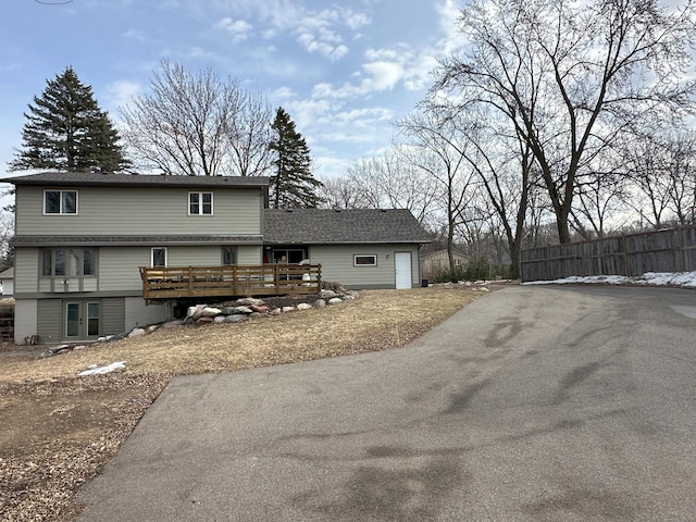 view of front of house with a garage, driveway, fence, a shingled roof, and a wooden deck