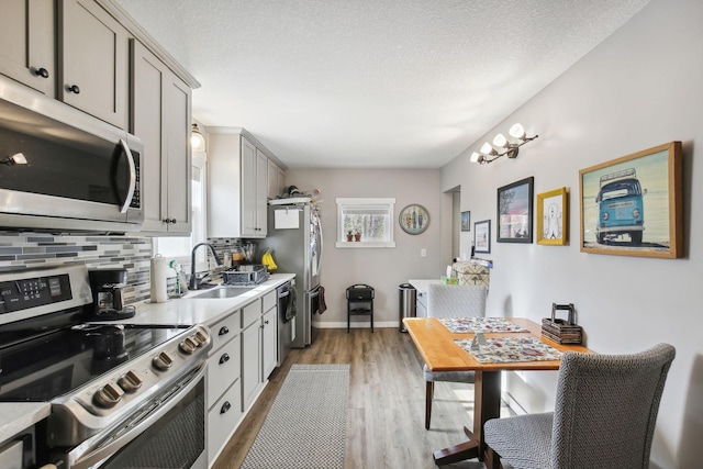 kitchen with sink, appliances with stainless steel finishes, light hardwood / wood-style flooring, gray cabinetry, and decorative backsplash