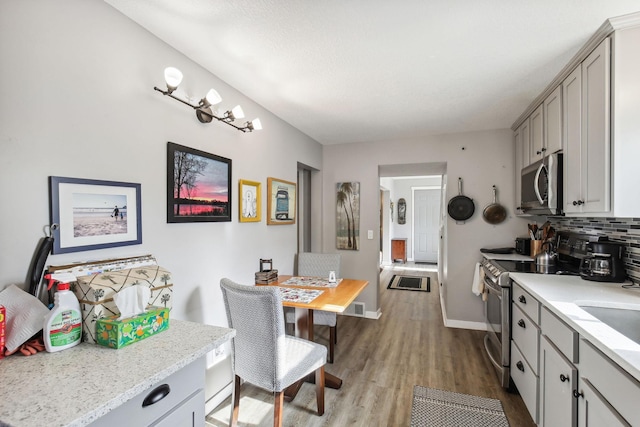 kitchen with stainless steel appliances, tasteful backsplash, light stone countertops, gray cabinetry, and light wood-type flooring