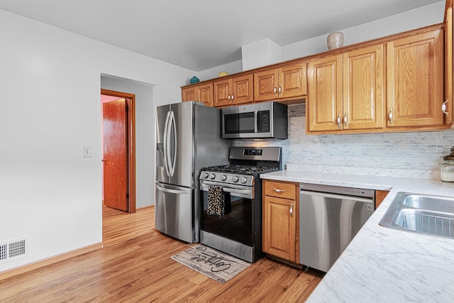 kitchen with appliances with stainless steel finishes, backsplash, and light hardwood / wood-style flooring