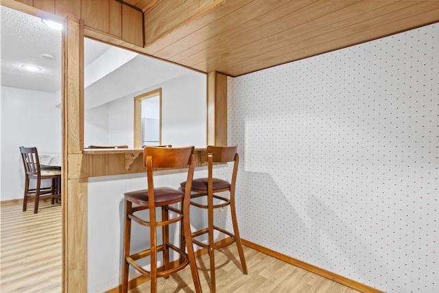 interior space featuring light wood-type flooring, wooden ceiling, and indoor bar