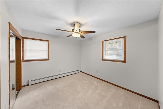 spare room featuring ceiling fan, light colored carpet, a wealth of natural light, and a baseboard heating unit