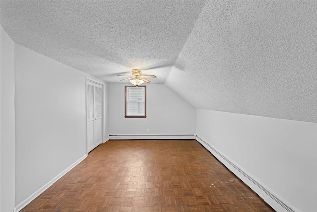 additional living space with lofted ceiling, a textured ceiling, parquet floors, and a baseboard heating unit