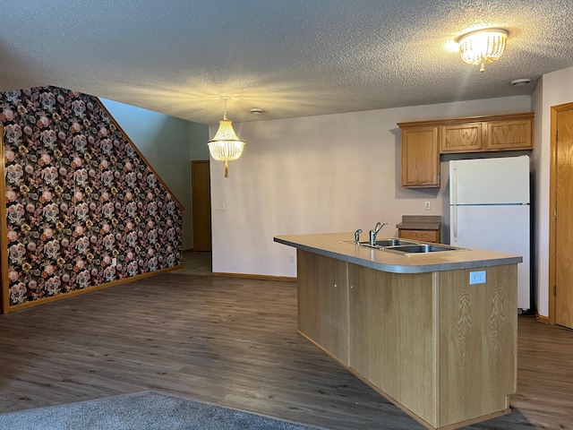 kitchen featuring wood-type flooring, a textured ceiling, sink, an island with sink, and white fridge