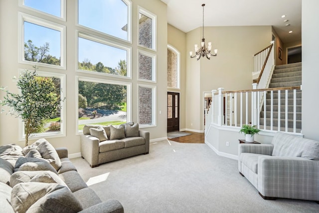 carpeted living area with a notable chandelier, a high ceiling, a healthy amount of sunlight, stairs, and baseboards