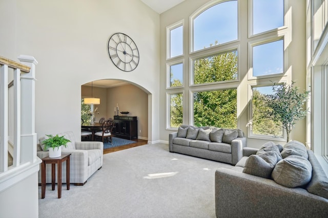 living area featuring arched walkways, plenty of natural light, carpet flooring, and a towering ceiling