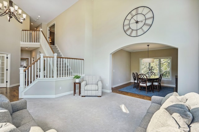 living room featuring a chandelier, carpet floors, a towering ceiling, baseboards, and stairs