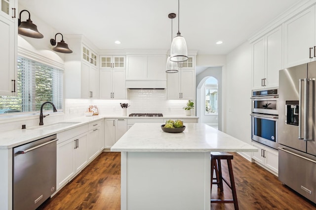 kitchen featuring tasteful backsplash, arched walkways, a kitchen island, appliances with stainless steel finishes, and a sink