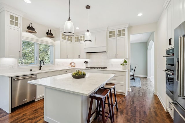 kitchen with a center island, arched walkways, stainless steel appliances, custom range hood, and a sink