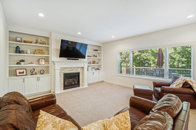 living room with a stone fireplace, built in shelves, recessed lighting, light colored carpet, and baseboards