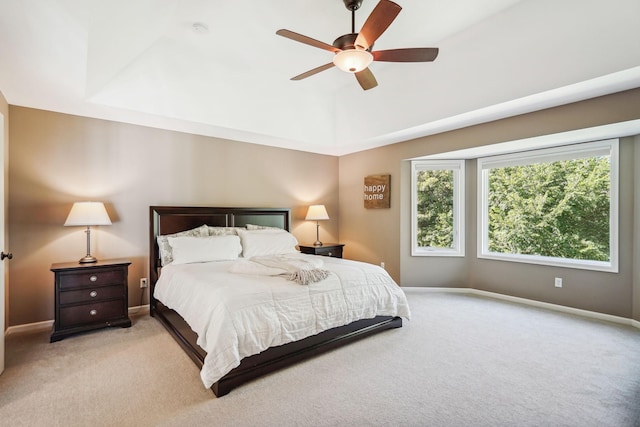 bedroom featuring light carpet, a raised ceiling, a ceiling fan, and baseboards