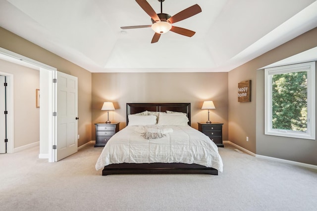 bedroom with a ceiling fan, a raised ceiling, light colored carpet, and baseboards