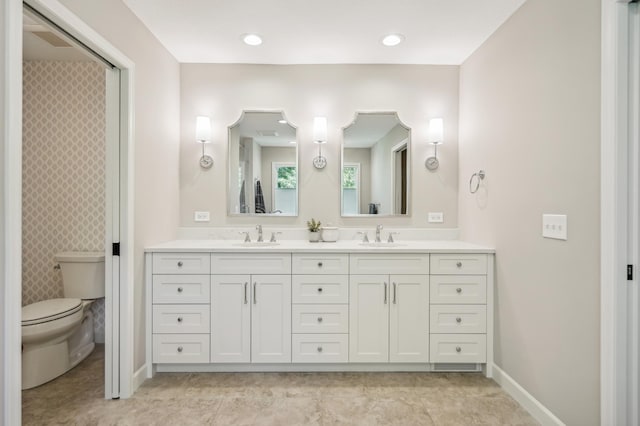 bathroom with double vanity, a sink, toilet, and baseboards