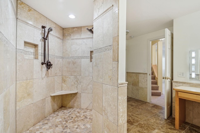 bathroom featuring a wainscoted wall, tiled shower, tile walls, and vanity