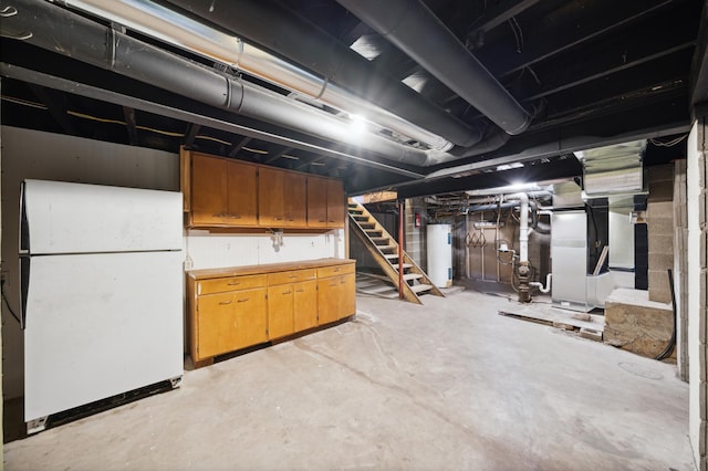 basement featuring heating unit, electric water heater, and white fridge