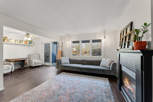 living room featuring dark wood-type flooring, ceiling fan, and a textured ceiling