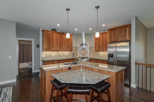 kitchen with stainless steel appliances, dark hardwood / wood-style flooring, a kitchen island with sink, wall chimney range hood, and pendant lighting