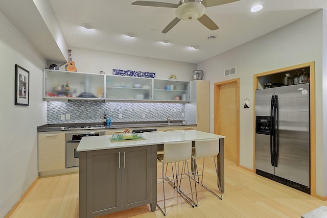 kitchen with appliances with stainless steel finishes, tasteful backsplash, ceiling fan, light hardwood / wood-style flooring, and a kitchen island