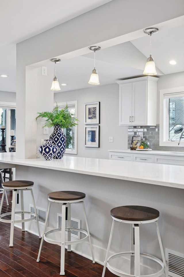 kitchen featuring backsplash, a kitchen bar, hanging light fixtures, and white cabinets