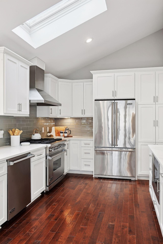 kitchen with wall chimney exhaust hood, white cabinetry, high quality appliances, vaulted ceiling with skylight, and decorative backsplash