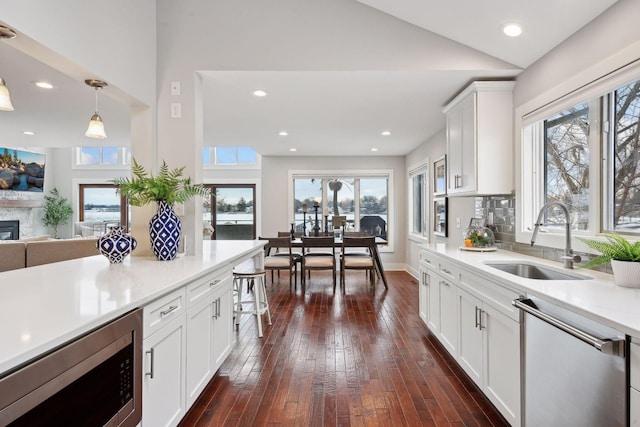 kitchen with a stone fireplace, sink, white cabinetry, pendant lighting, and stainless steel appliances